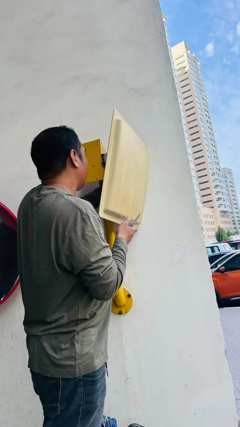 Technician fitting an access control reader on a yellow bracket on a pillar beside a convex mirror in Ajman