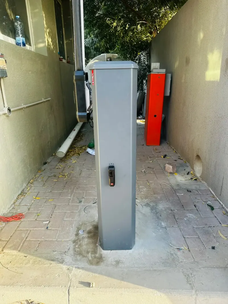 Grey BFT gate barrier cabinet on a new concrete base في a narrow paved lane in Ras Al Khaimah