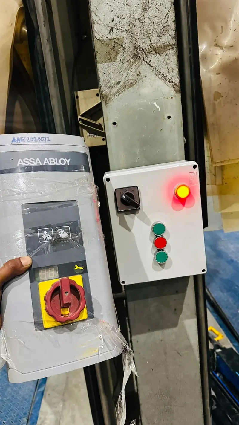 New ASSA ABLOY dock leveler controller held beside an existing wall control box with selector and push buttons