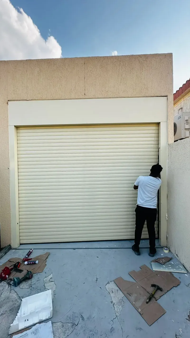 Technician finishing the side of a cream rolling shutter installed in a house opening in Fujairah